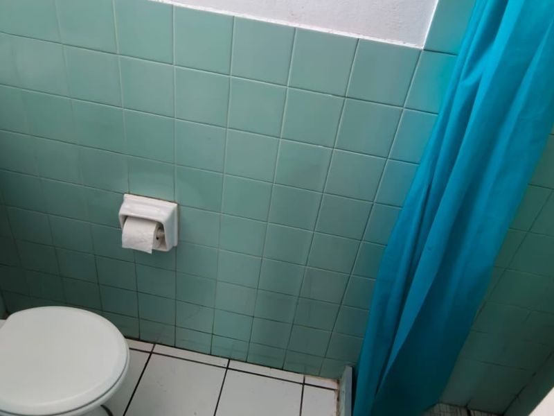 A compact bathroom featuring dated mint green wall tiles, white floor tiles, and standard sanitary fixtures.