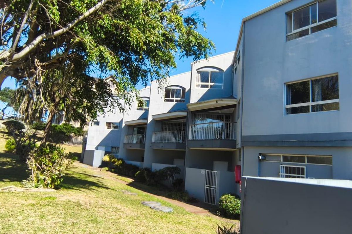 Rear elevation of a multi-story apartment complex featuring private balconies, security gates, and a landscaped garden area.
