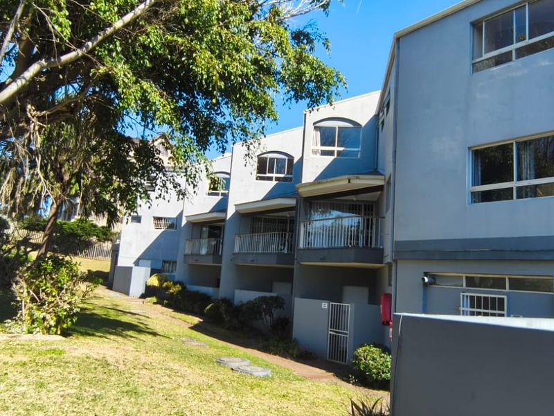 Rear elevation of a multi-story apartment complex featuring private balconies, security gates, and a landscaped garden area.
