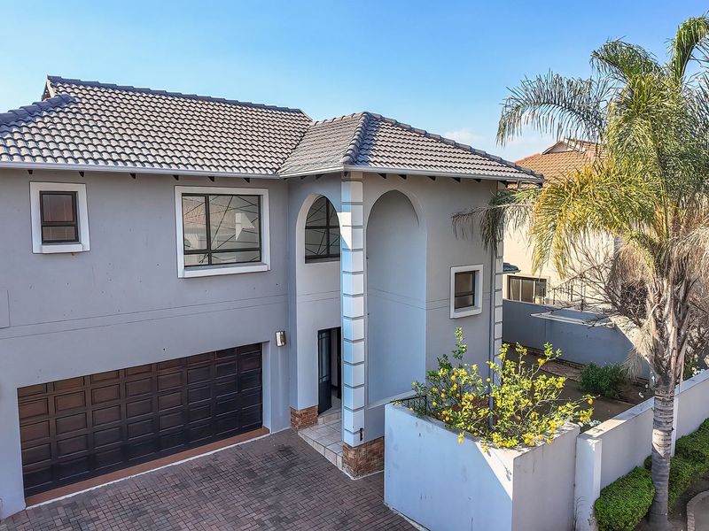 A well-maintained double-story house featuring a tiled roof, a paved driveway, and a double garage with an arched entrance.