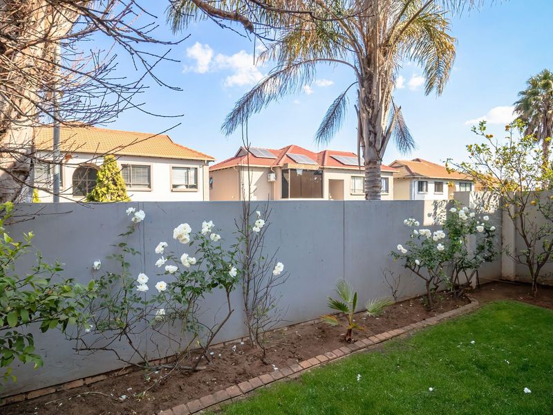 A well-maintained private garden featuring a neat lawn, established rose bushes, and a solid boundary wall providing privacy.