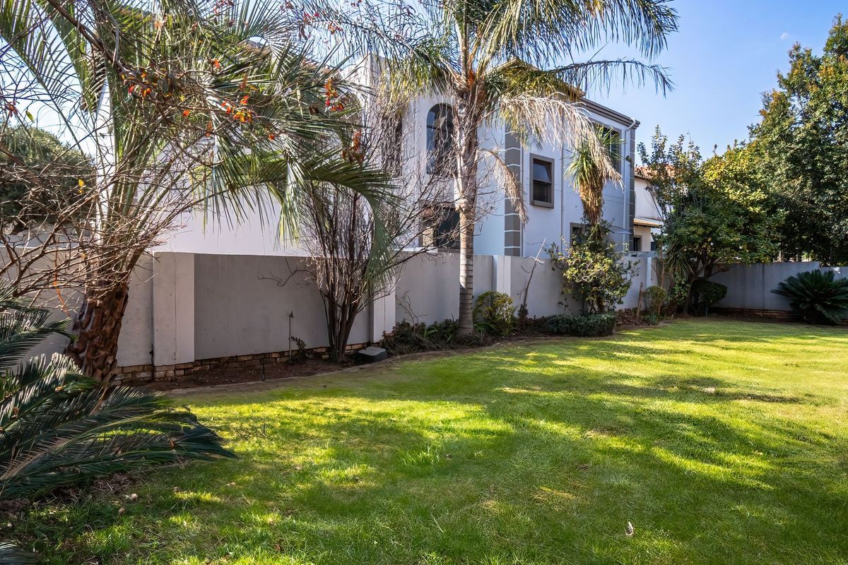 A spacious rear garden featuring a well-maintained lawn, mature trees, and a view of the multi-story residential building's rear facade.