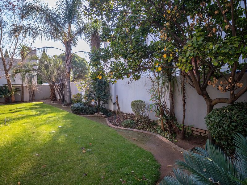 A private rear garden featuring a well-maintained lawn, established trees, and perimeter boundary walls with brick edging.