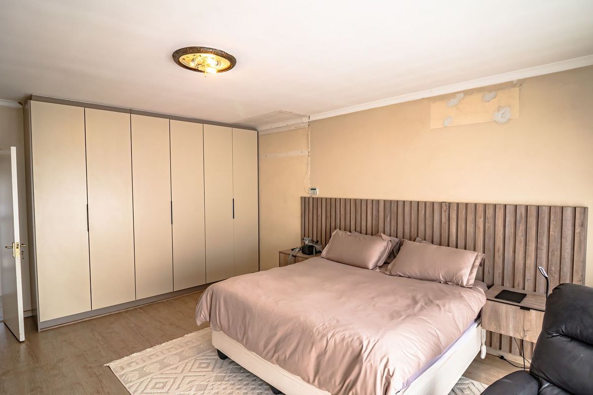 Spacious bedroom featuring extensive built-in cupboards, a timber slat headboard, and laminate flooring, requiring minor cosmetic wall repairs.