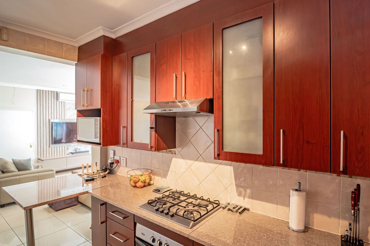 A functional kitchen featuring warm-toned wooden cabinetry, stone countertops, a gas hob with extractor fan, and a built-in oven, seamlessly flowing into the living area.