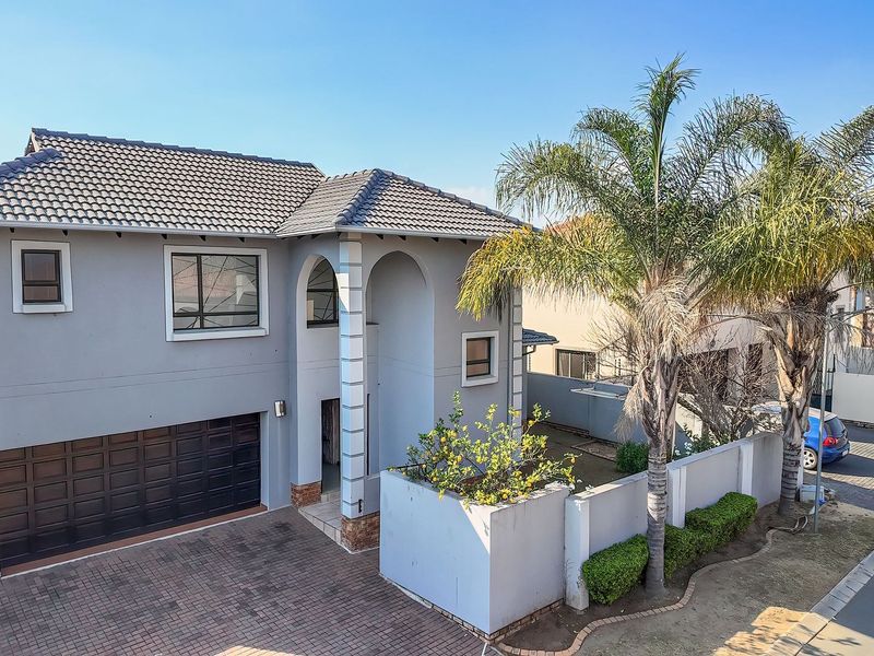 A well-maintained double-story residential property featuring a tiled roof, arched entrance, and a paved driveway leading to a double garage.