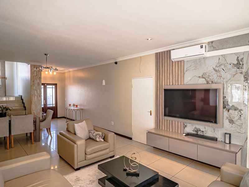 Spacious open-plan living and dining area featuring tiled floors, a modern marble-look feature wall with integrated cabinetry, and a split-system air conditioner.