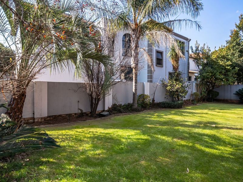 A spacious rear garden featuring a well-maintained lawn, mature trees, and a view of the multi-story residential building's rear facade.