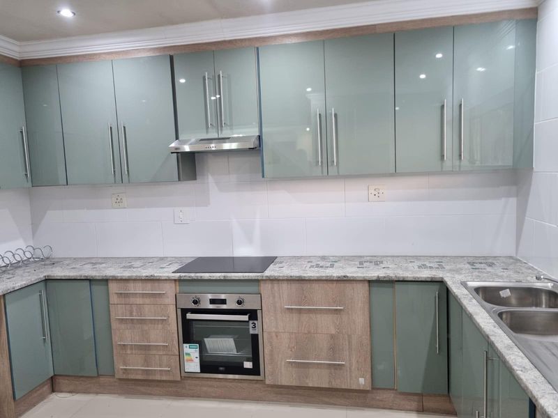 Modern kitchen featuring sleek two-tone cabinetry, stone countertops, integrated electric hob, built-in oven, extractor fan, and a double bowl sink with tiled backsplash.
