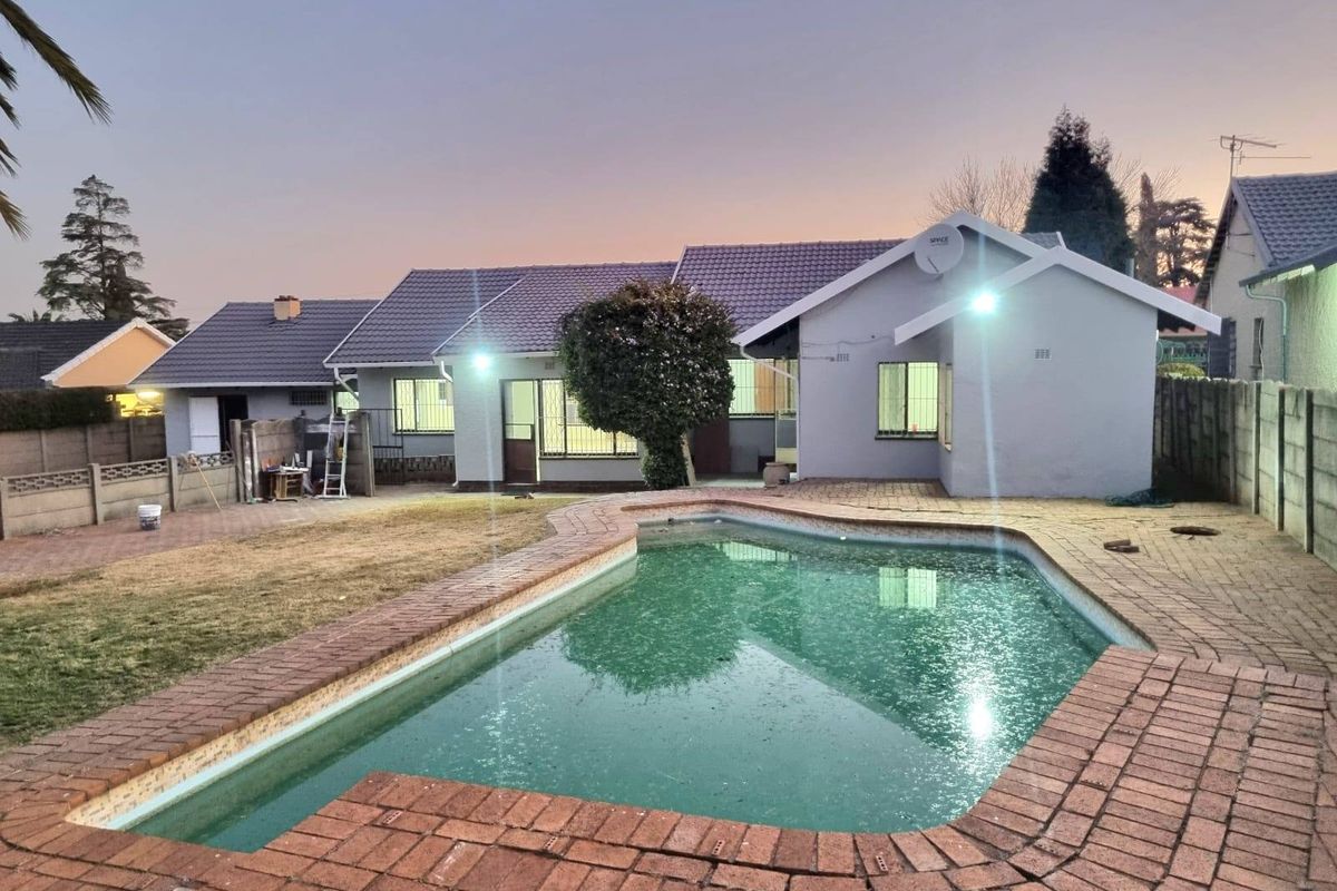 Rear view of the property featuring a swimming pool, brick-paved patio area, and a tiled roof structure at dusk.