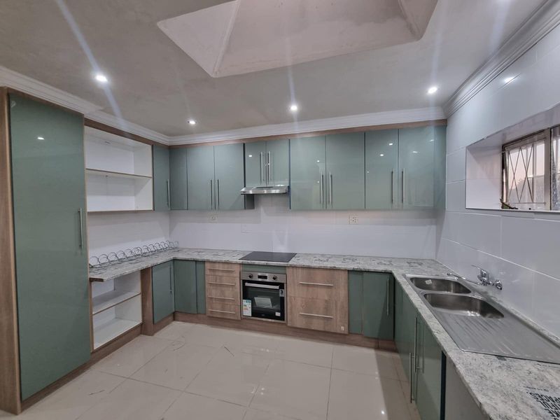 Modern kitchen featuring high-gloss cabinetry, granite countertops, integrated oven and hob, and a double stainless steel sink with tiled flooring.