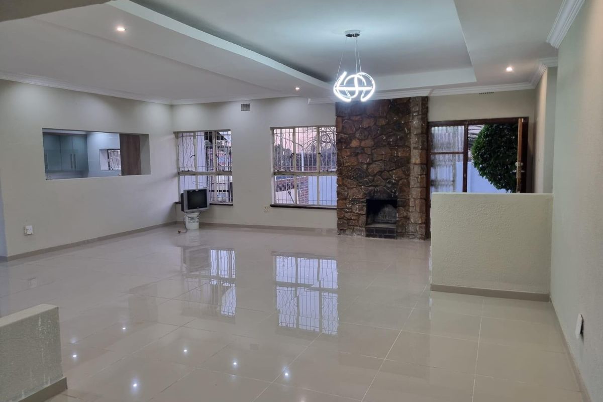 Spacious open-plan living area featuring polished tile floors, a prominent stone fireplace, and a modern recessed ceiling design with integrated lighting.