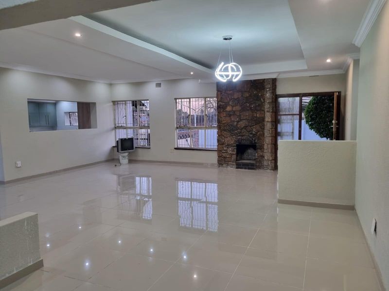 Spacious open-plan living area featuring polished tile floors, a prominent stone fireplace, and a modern recessed ceiling design with integrated lighting.