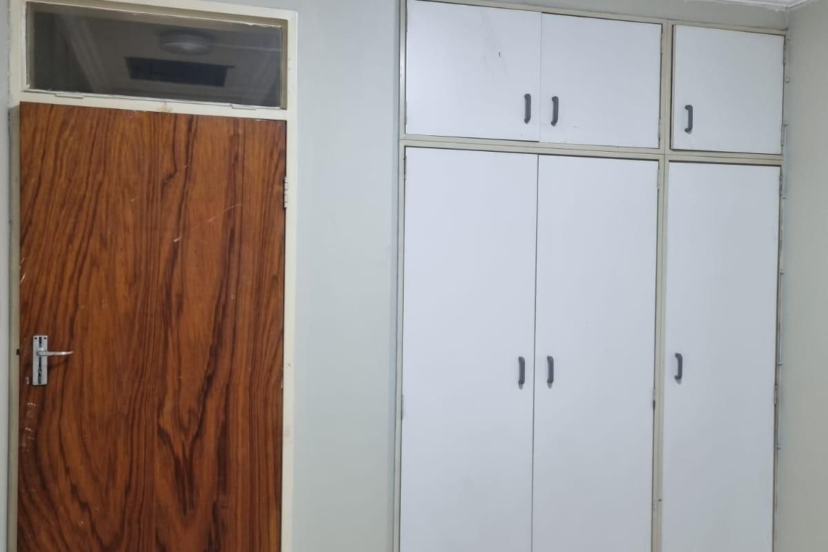 A bedroom featuring built-in cupboards, tiled flooring, and a wooden door with a transom window above.
