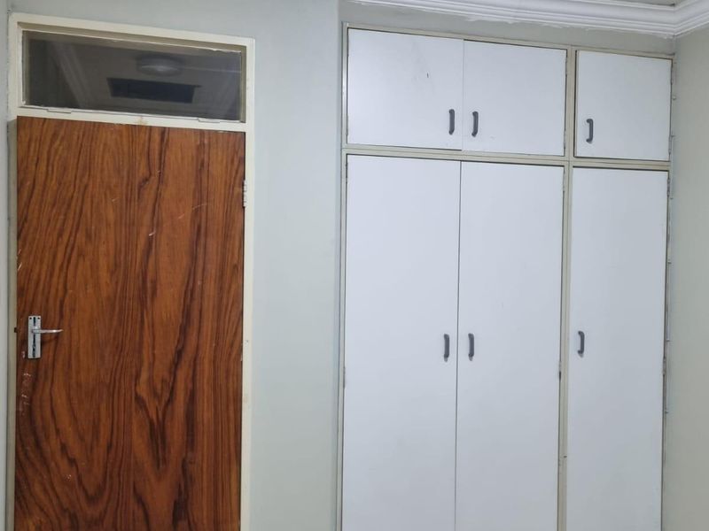 A bedroom featuring built-in cupboards, tiled flooring, and a wooden door with a transom window above.
