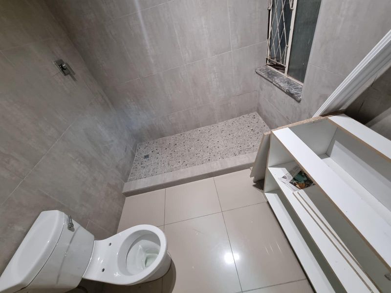 A modern bathroom featuring a walk-in shower with stone-look tiling, a toilet, and unfinished shelving units awaiting final installation.