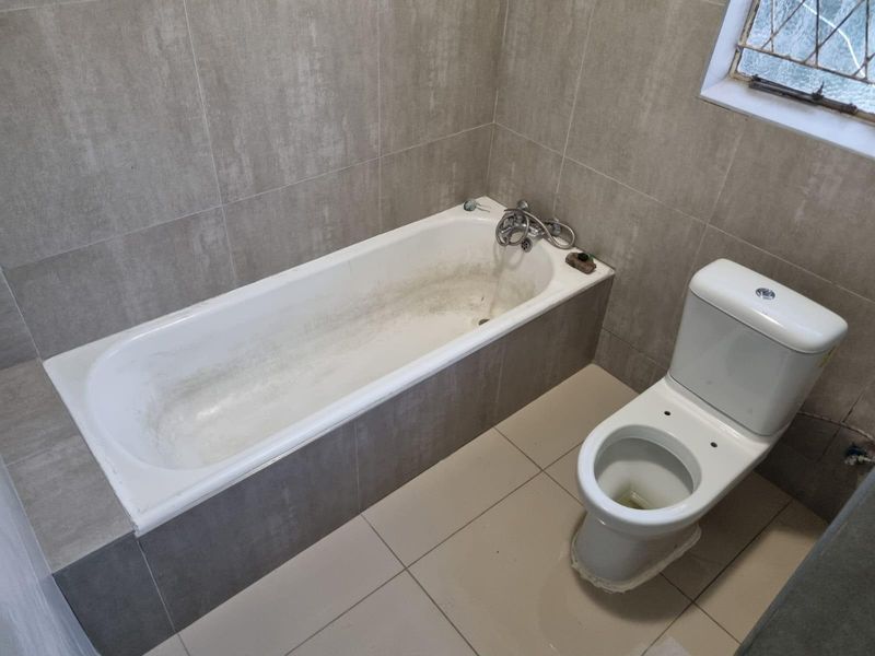 A functional bathroom featuring a built-in bathtub and toilet with neutral wall and floor tiling, requiring some maintenance and cosmetic updates.