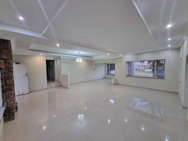 Spacious, open-plan living area featuring polished porcelain floor tiles, a decorative stone feature wall, and a modern recessed ceiling with integrated downlights.