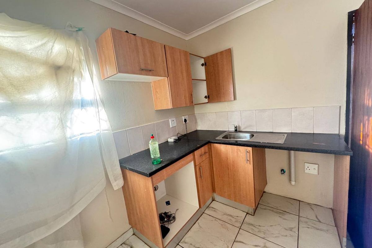 A compact kitchen featuring laminate cabinetry, a stainless steel sink, tiled backsplash, and tiled flooring, currently in need of minor repairs and updates.