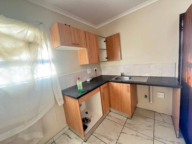 A compact kitchen featuring laminate cabinetry, a stainless steel sink, tiled backsplash, and tiled flooring, currently in need of minor repairs and updates.