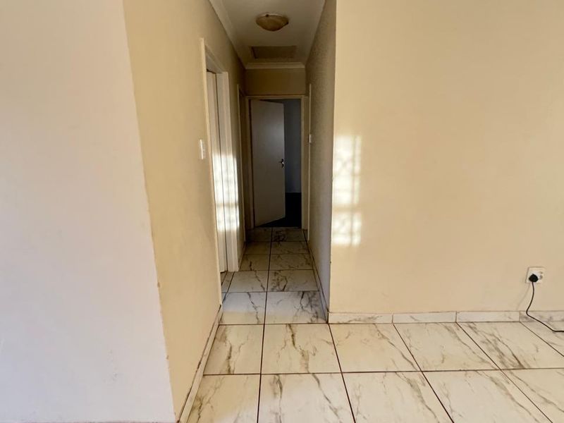 A bright, empty hallway featuring marble-look ceramic floor tiles and neutral wall finishes, providing access to adjacent rooms.