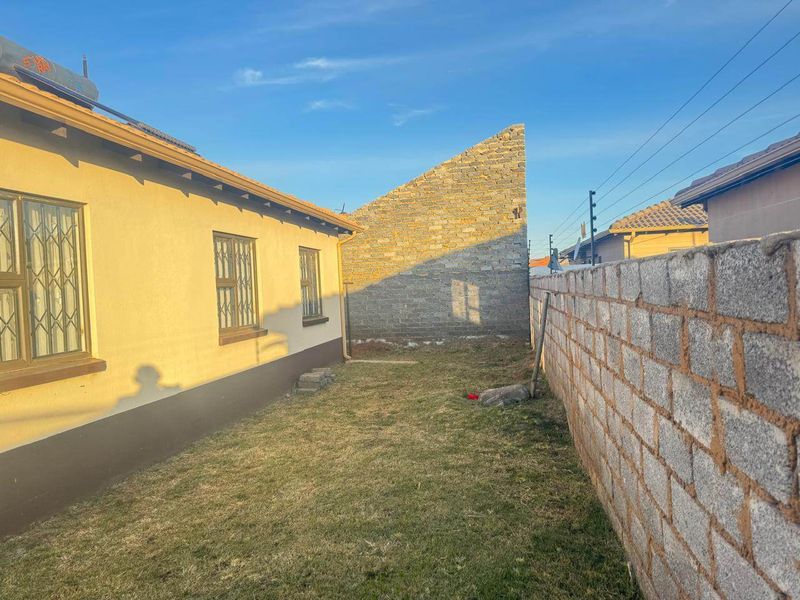 Rear exterior view showing a lawn area, perimeter wall with electric fencing, and a partially finished stone feature wall.