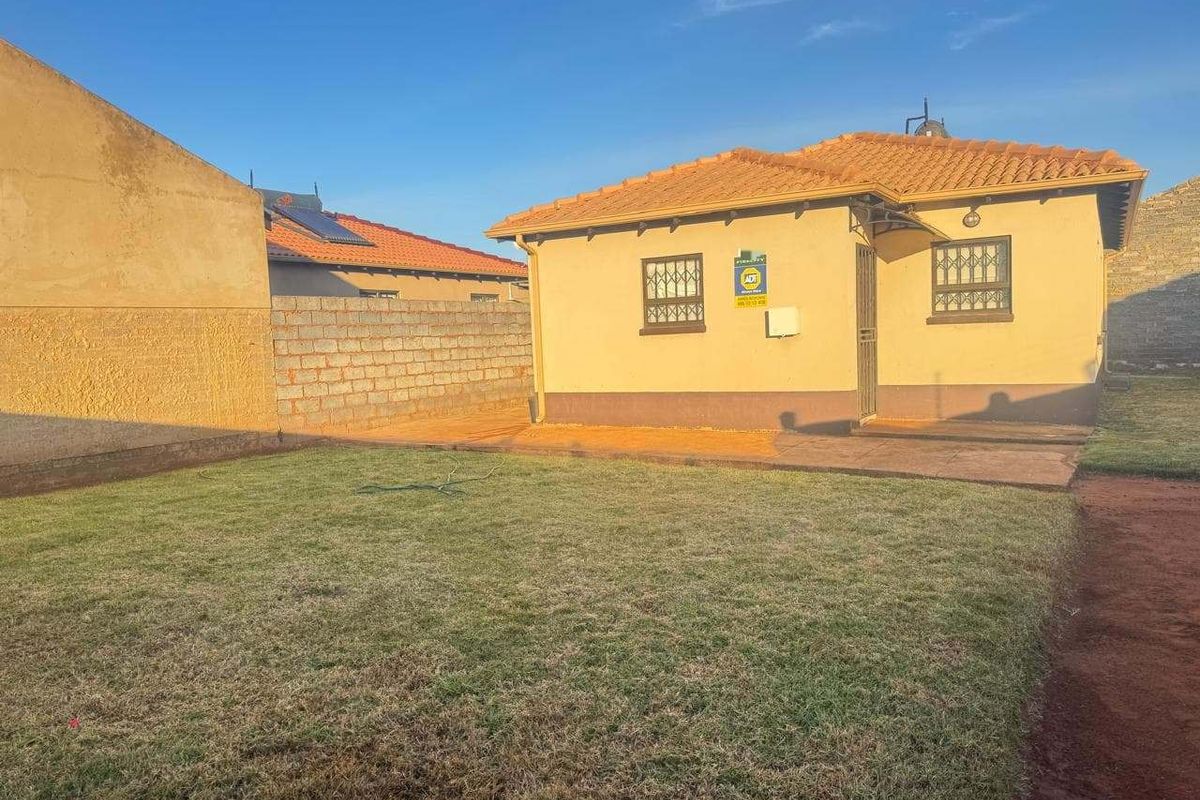 Rear view of the property featuring a tiled roof, security bars on windows, a security gate, and a private lawn area with boundary walls.