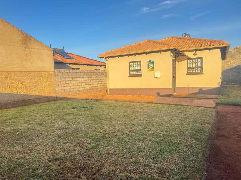 Rear view of the property featuring a tiled roof, security bars on windows, a security gate, and a private lawn area with boundary walls.