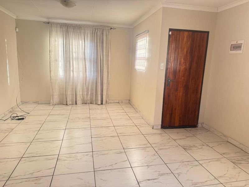 A bright, empty living area featuring neutral walls, marble-look tiled flooring, and a solid wooden entrance door.