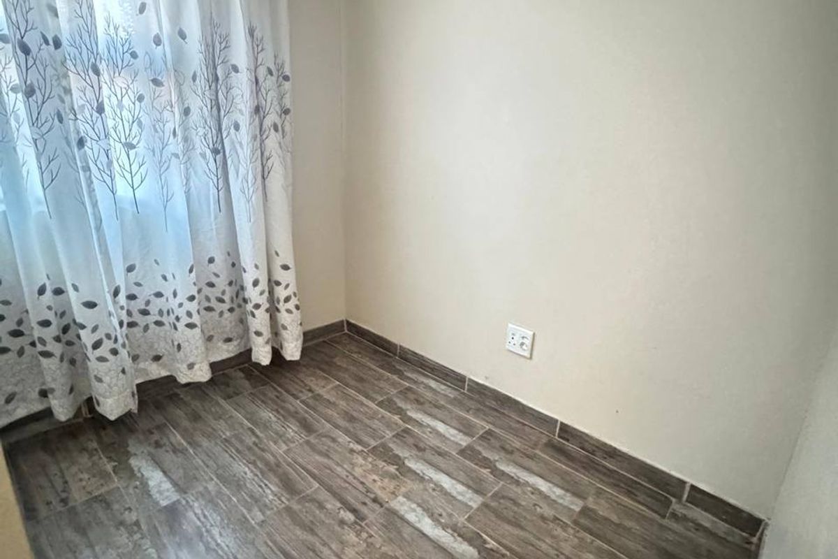 A clean, empty bedroom featuring modern wood-look tiled flooring and neutral wall finishes, ready for personalization.
