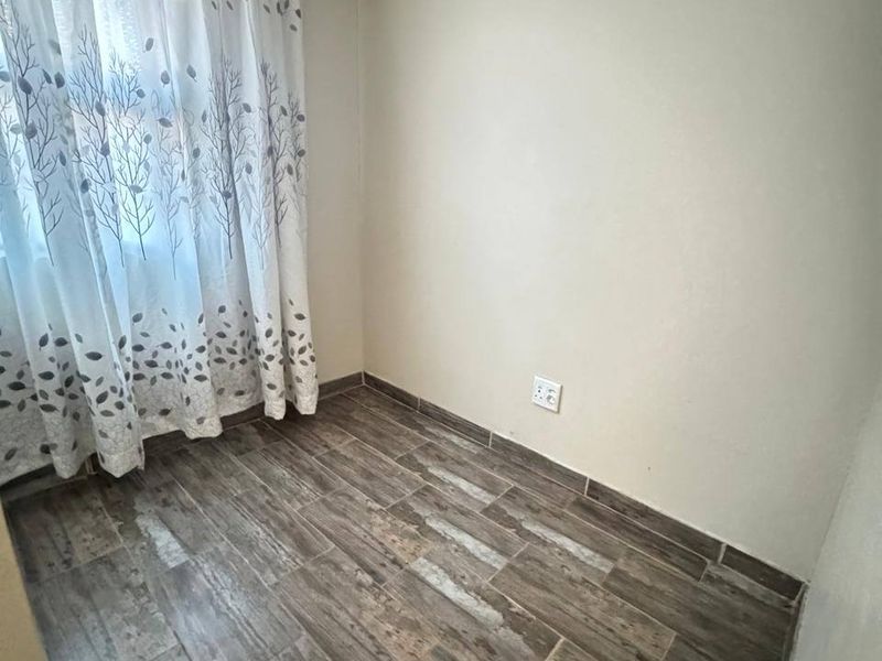 A clean, empty bedroom featuring modern wood-look tiled flooring and neutral wall finishes, ready for personalization.