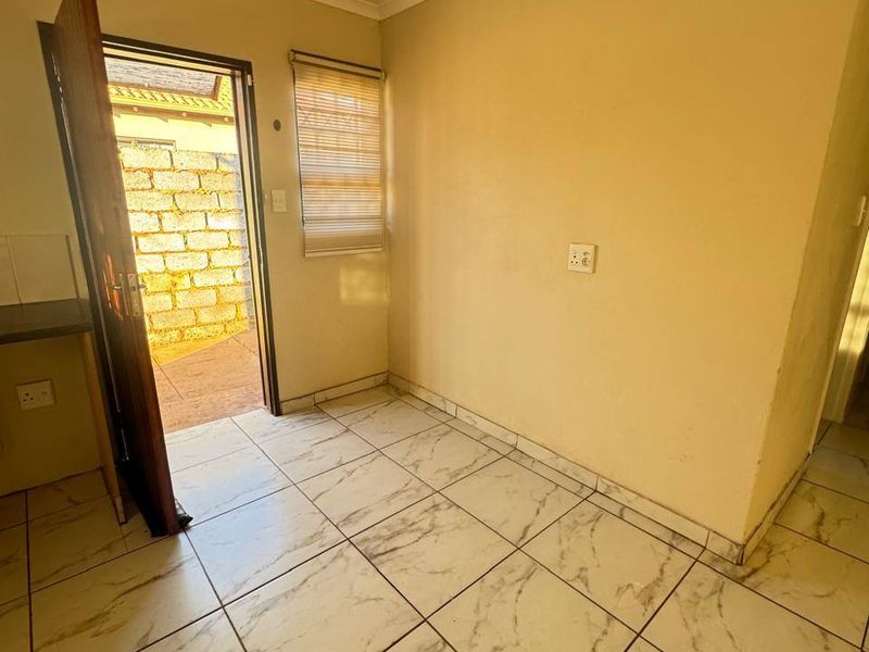 A compact, empty kitchen area featuring marble-look floor tiles, a roller blind, and direct access to an outdoor space.