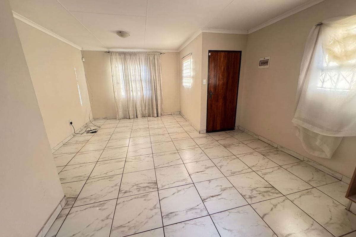 A spacious, empty living area featuring marble-look ceramic floor tiles, neutral walls, and a solid wooden door.