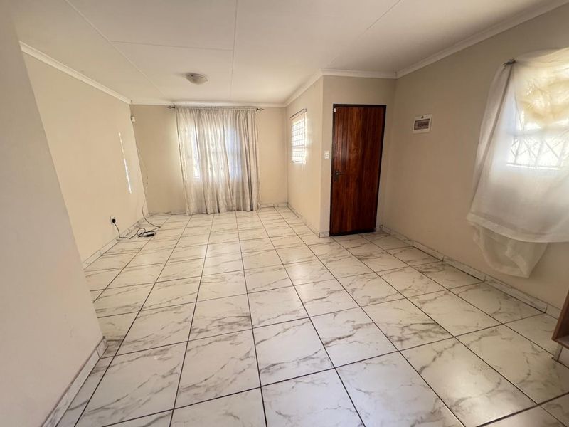 A spacious, empty living area featuring marble-look ceramic floor tiles, neutral walls, and a solid wooden door.