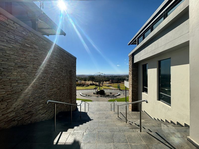 An exterior view of a modern apartment complex entrance featuring stone-clad walls, stainless steel handrails, and a tiled staircase leading to a landscaped driveway.