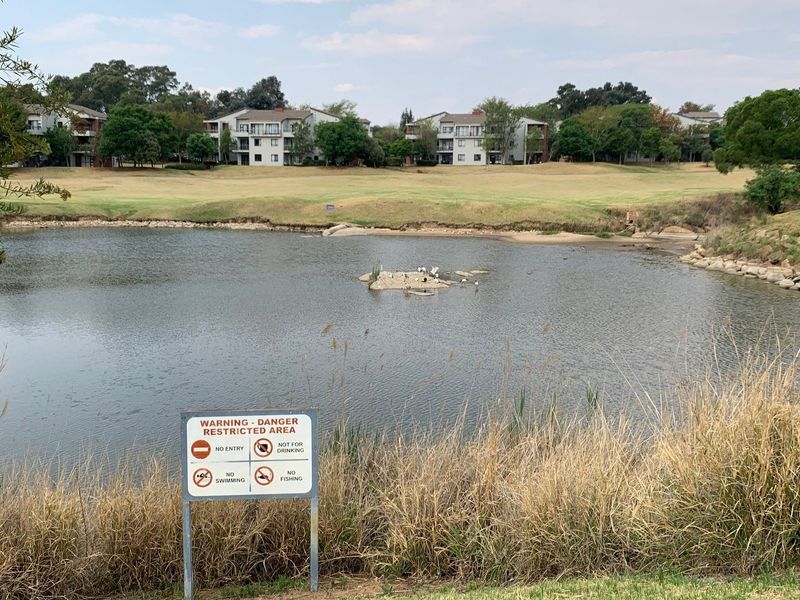 A scenic view overlooking a tranquil lake with apartment buildings situated in the background within a landscaped estate setting.