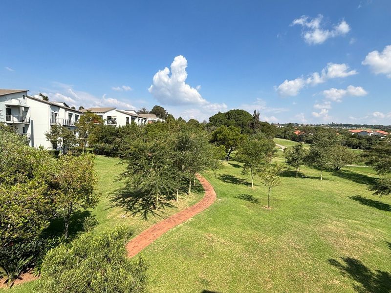 A scenic elevated view overlooking a well-maintained communal garden area with mature trees and a winding paved pathway within the apartment complex.