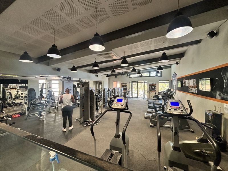 A well-equipped apartment complex gym featuring rubberized flooring, acoustic ceiling panels, and professional-grade fitness equipment in a spacious, well-lit environment.