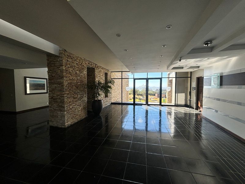 Spacious modern entrance lobby featuring a stone-clad feature wall, high-gloss tiled flooring, and large glass doors providing natural light and exterior views.