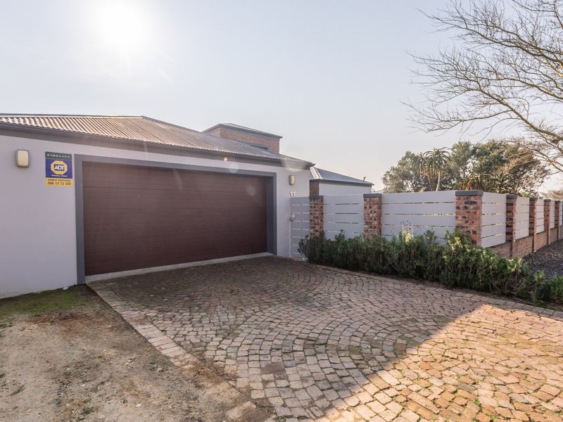 Front exterior view featuring a double garage with a cobblestone driveway and a secure brick and timber boundary wall.