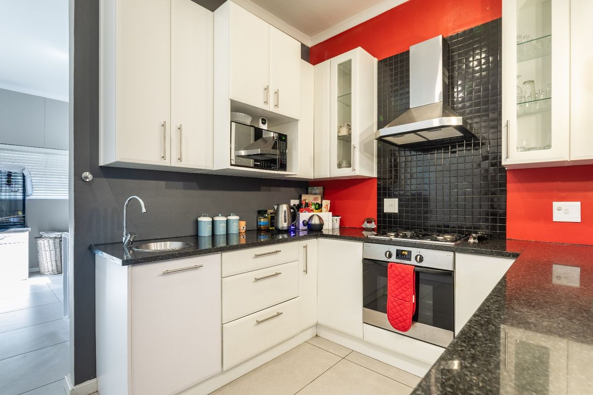 Modern kitchen featuring white cabinetry, granite countertops, stainless steel appliances, and a striking red and black tiled backsplash.