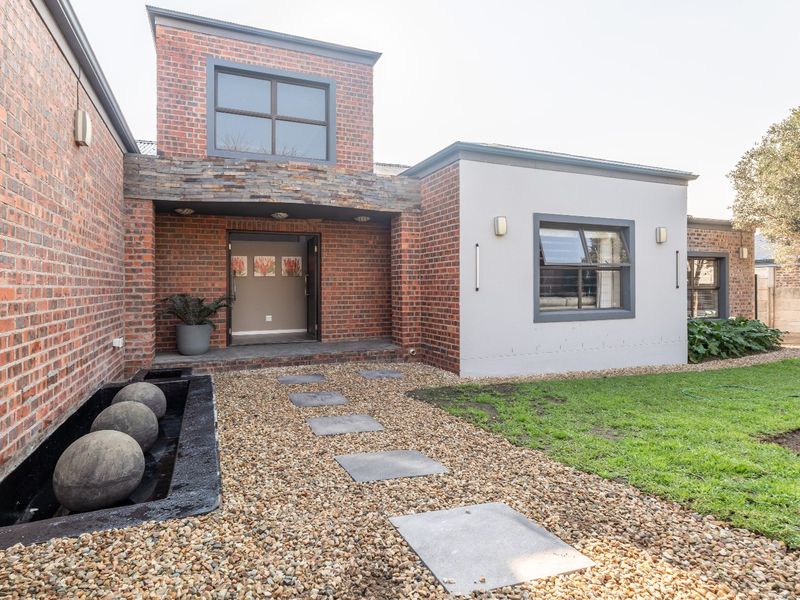 Modern front facade featuring exposed brickwork, stone accents, a landscaped garden with a water feature, and a paved entrance pathway.