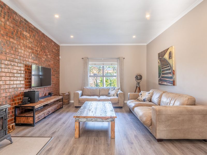 Spacious living room featuring an exposed brick wall, a cast iron wood-burning fireplace, and modern laminate flooring with recessed lighting.