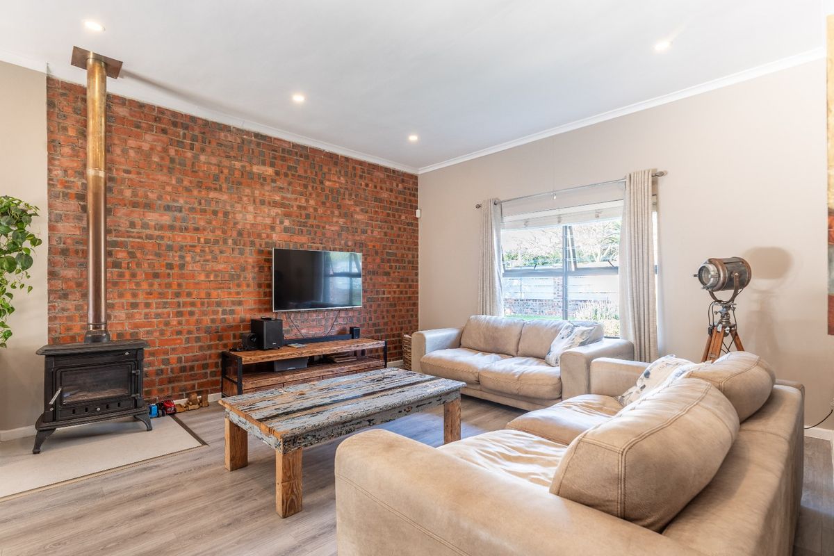 Spacious living room featuring an exposed brick wall, a freestanding wood-burning fireplace, and modern laminate flooring with recessed lighting.