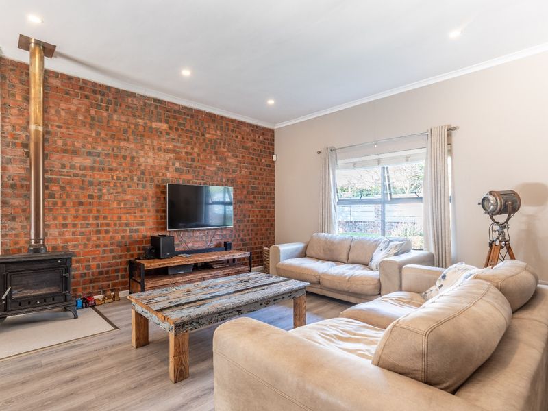Spacious living room featuring an exposed brick wall, a freestanding wood-burning fireplace, and modern laminate flooring with recessed lighting.