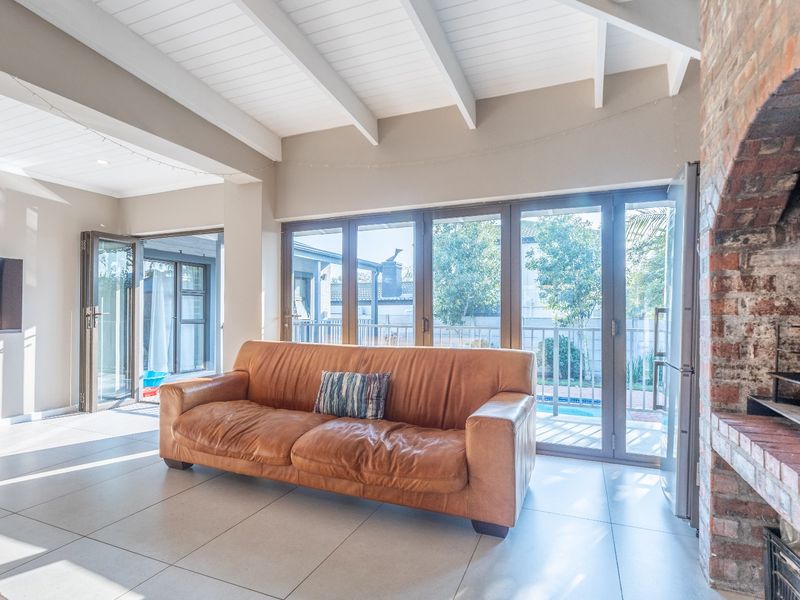 Spacious living area featuring exposed beam ceilings, tiled floors, a rustic brick fireplace, and large aluminium stacker doors opening to the outdoor pool area.