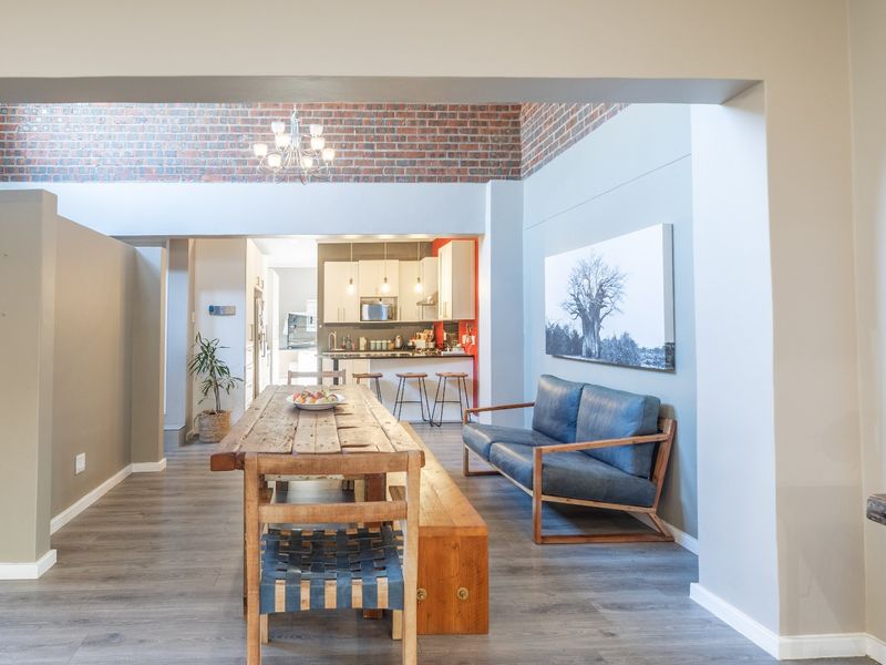 Spacious open-plan living and dining area featuring exposed brick accents, modern laminate flooring, and a functional kitchen with integrated cabinetry.