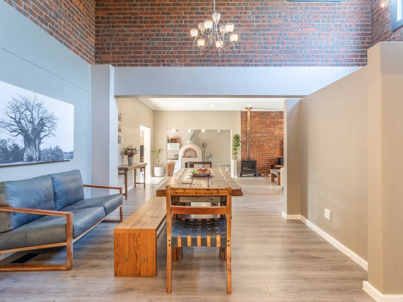 Spacious open-plan living and dining area featuring exposed brick walls, a wood-burning fireplace, and a built-in pizza oven with modern laminate flooring.