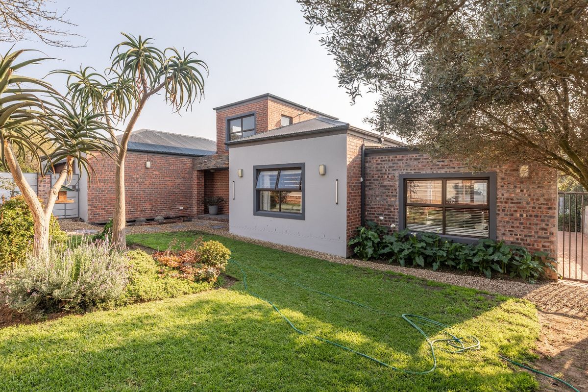 A well-maintained rear exterior view of a modern house featuring a mix of face brick and plastered finishes, set within a landscaped garden.