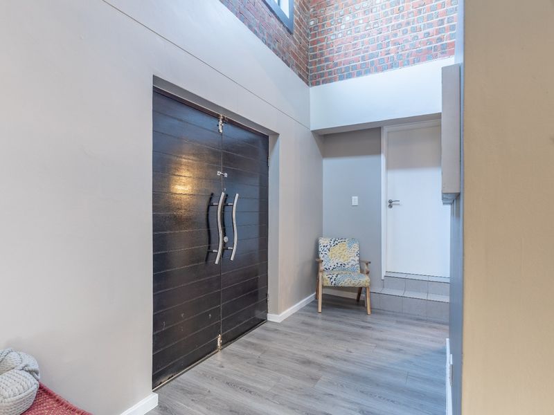 Spacious entrance hall featuring double doors, high ceilings with exposed brick accents, and modern laminate flooring.
